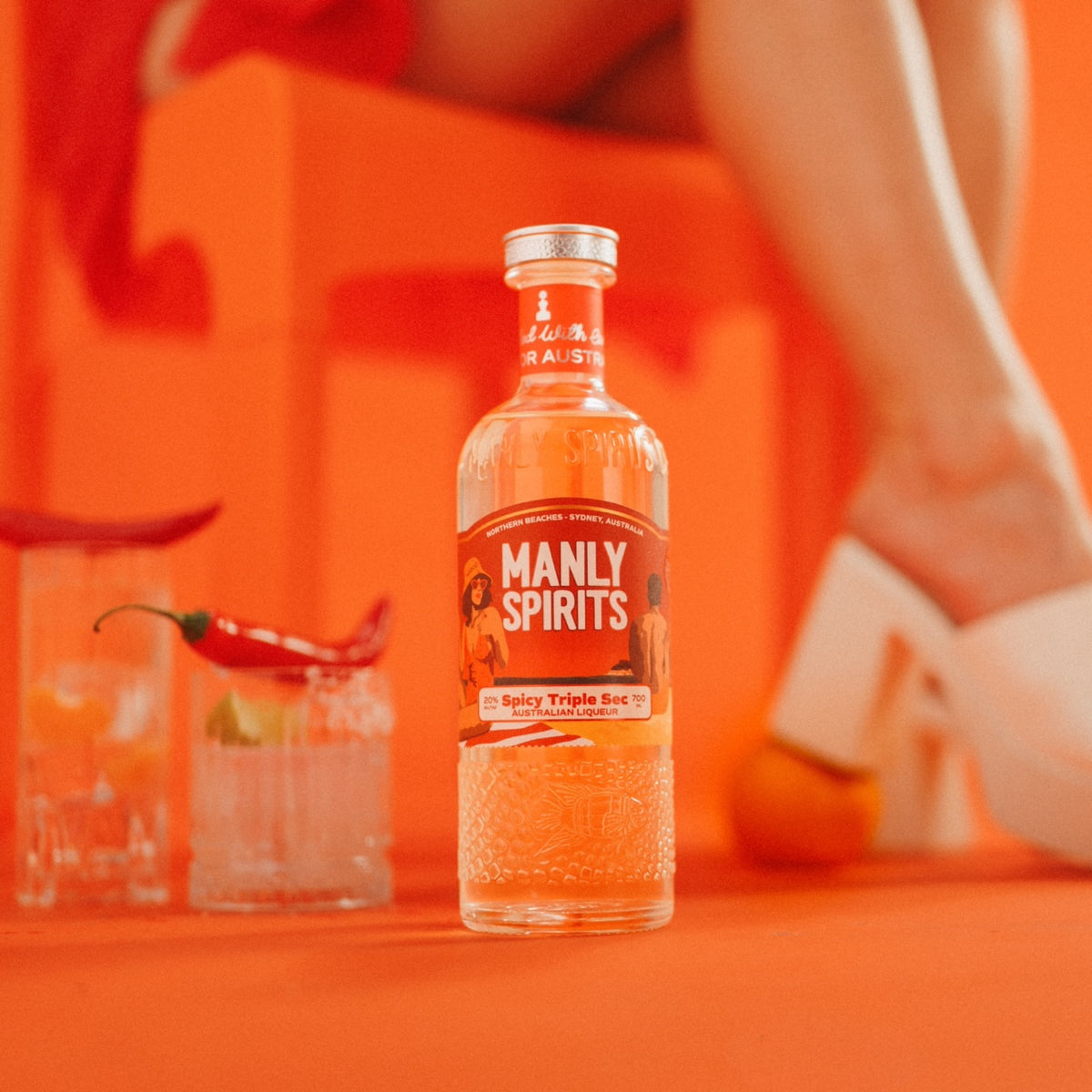 Manly Spirits Spicy Triple Sec beside two highballs topped with red chillies, on an orange set