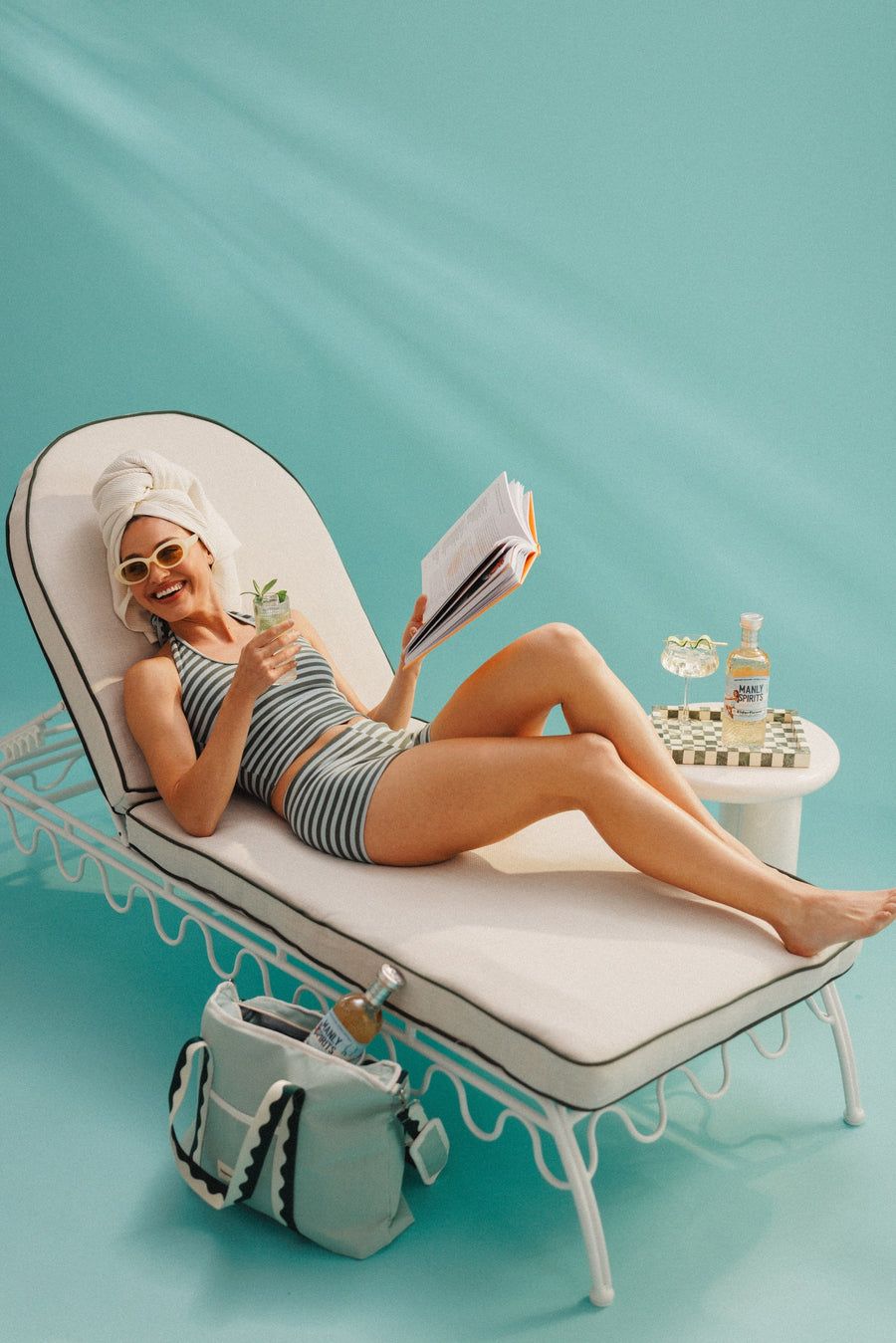 Reading on a sun lounger with a drink and a bottle of Elderflower Liqueur nearby