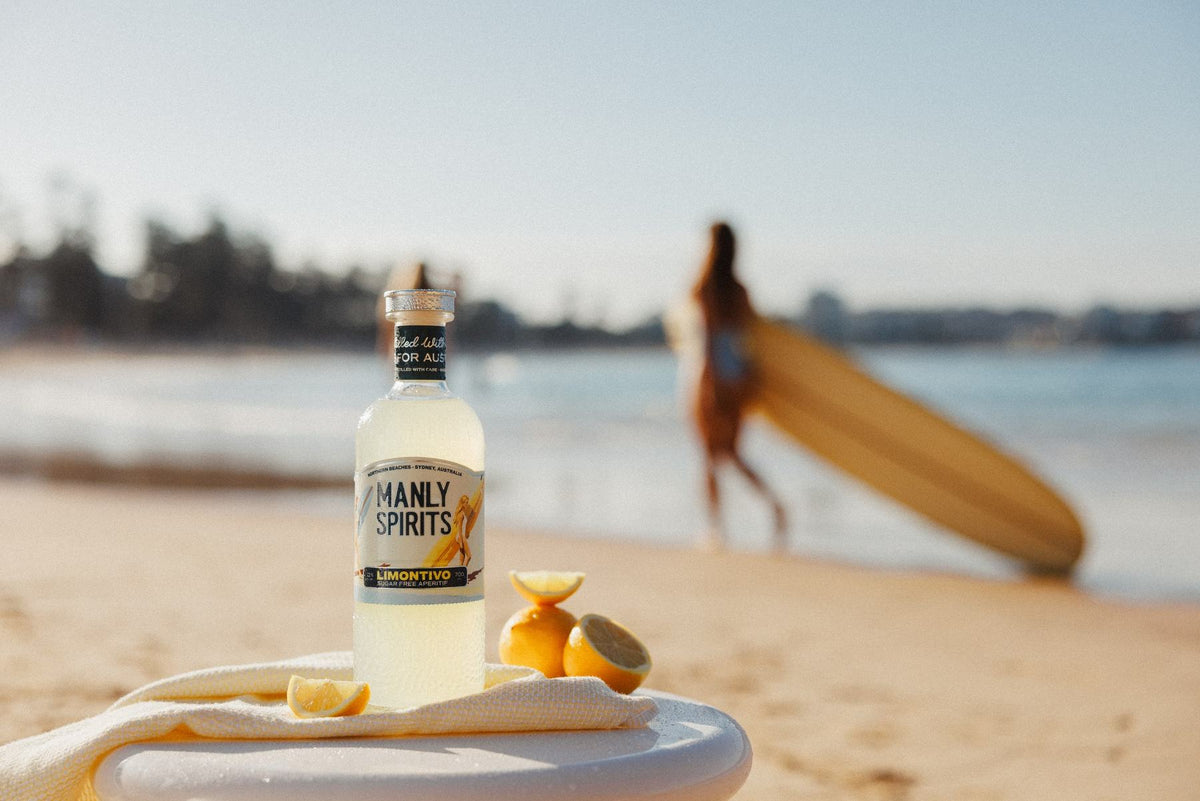Limontivo on a beach table with lemons, a surfer walking by