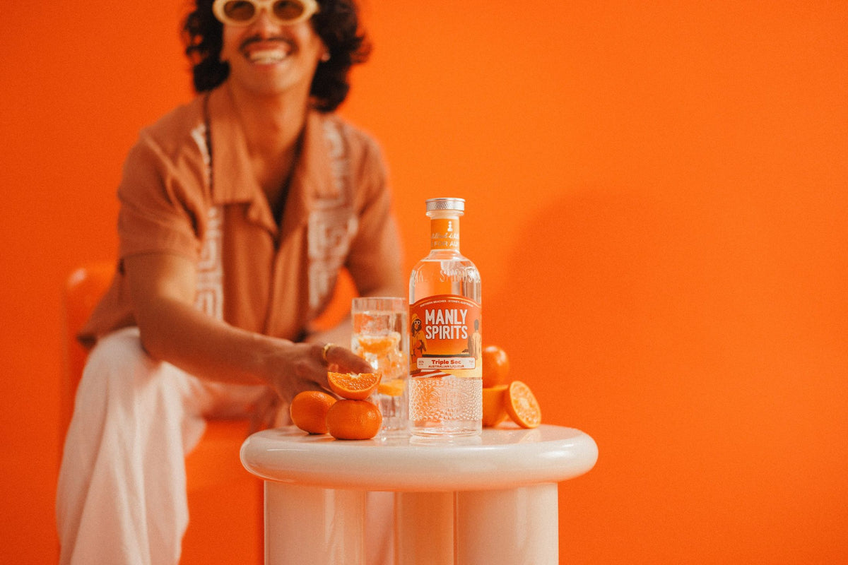 Mandarin Triple Sec bottle with mandarins and a drink on a white table against an orange wall